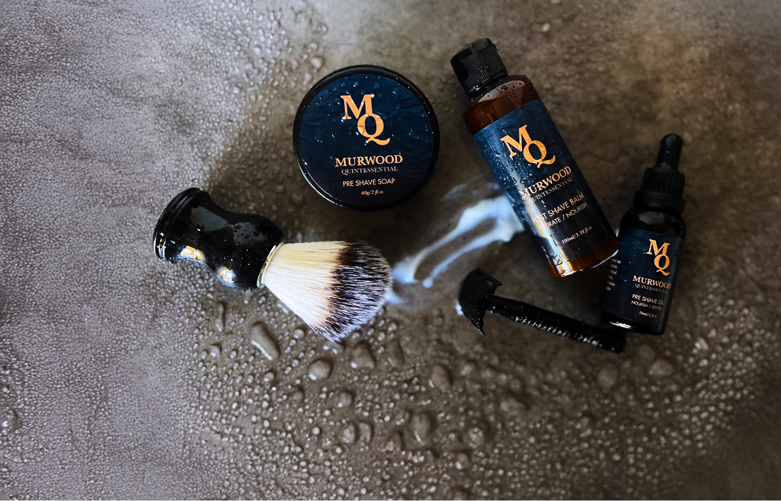 Shaving products including a Brush, Soap, Balm and Pre Shave Oil and Matte Black Razor on a wet surface branded 'Murwood Quintessential'.